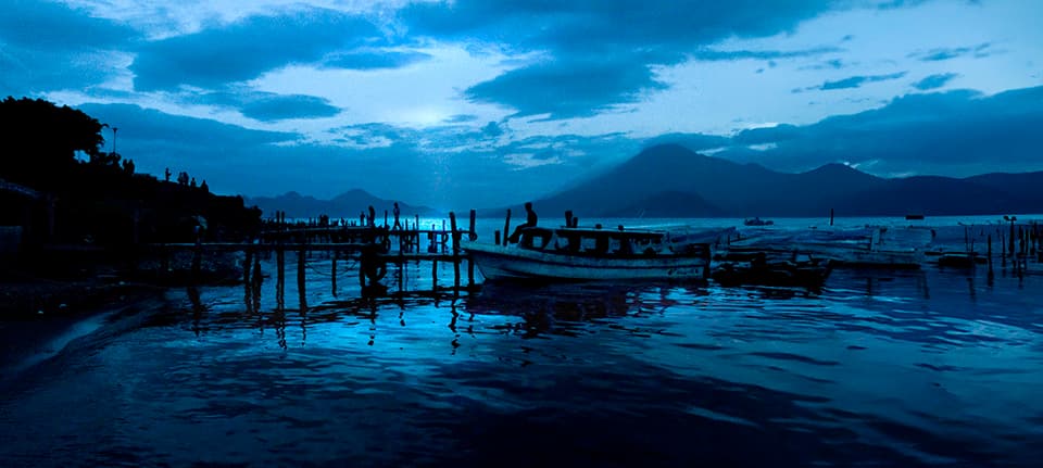 A mesmerizing blue hour scene captures the essence of tranquility. Boats rest peacefully on glassy waters, mirroring the dramatic sky above. This image invites you to pause and breathe in the calm of a perfect evening.
