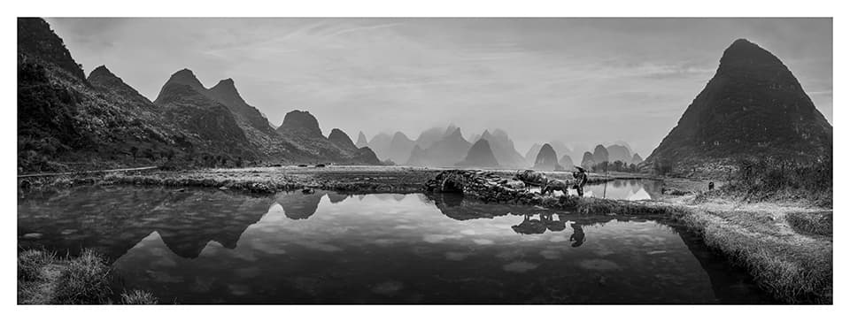 A breathtaking panorama of karst mountains reflects perfectly in still waters, creating a mirror world that blurs the line between earth and sky. This image captures the ethereal beauty of China's landscape, where jagged peaks seem to float in a dreamlike expanse, inviting viewers to lose themselves in nature's grandeur.