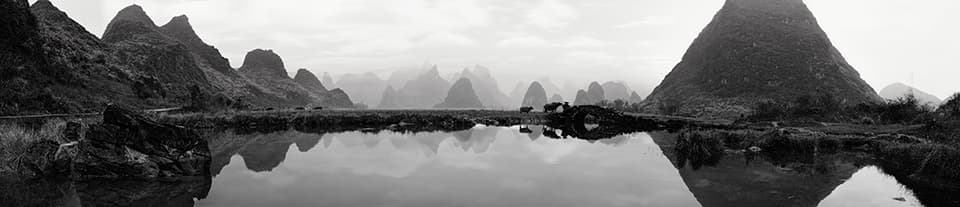 A vast panoramic view showcases the rhythmic repetition of karst mountains reflected in tranquil waters. The scene evokes a sense of timelessness, where the boundary between reality and reflection becomes indistinguishable. This image invites contemplation on the cyclical nature of existence and the enduring beauty of our natural world.