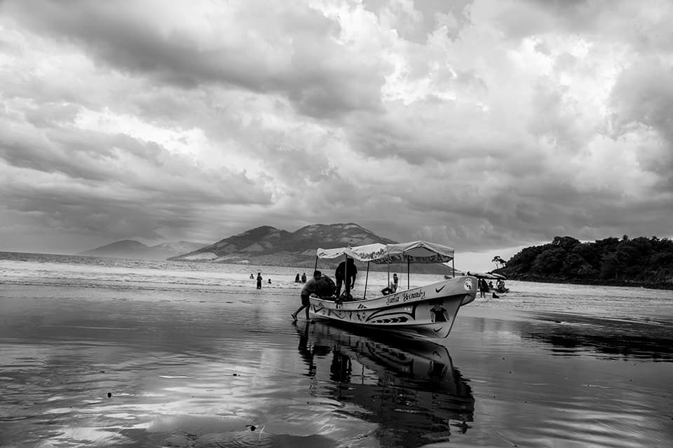 A solitary boat rests on a tranquil beach, set against a backdrop of misty mountains and brooding skies. This image captures the quiet moments before a storm, where the boundary between sea and sky blurs, creating a dreamlike atmosphere. It speaks to the calm that can be found even in the face of impending change.